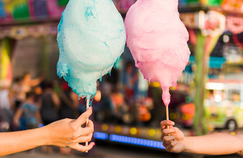 closeup of two people's arms holding cotton candy at a carnival